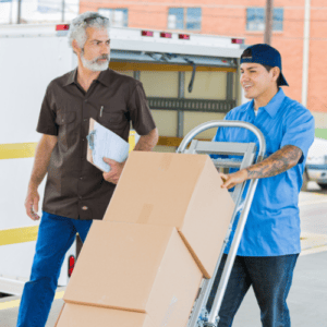 A supervisor with a clipboard overseeing a delivery while a colleague moves boxes